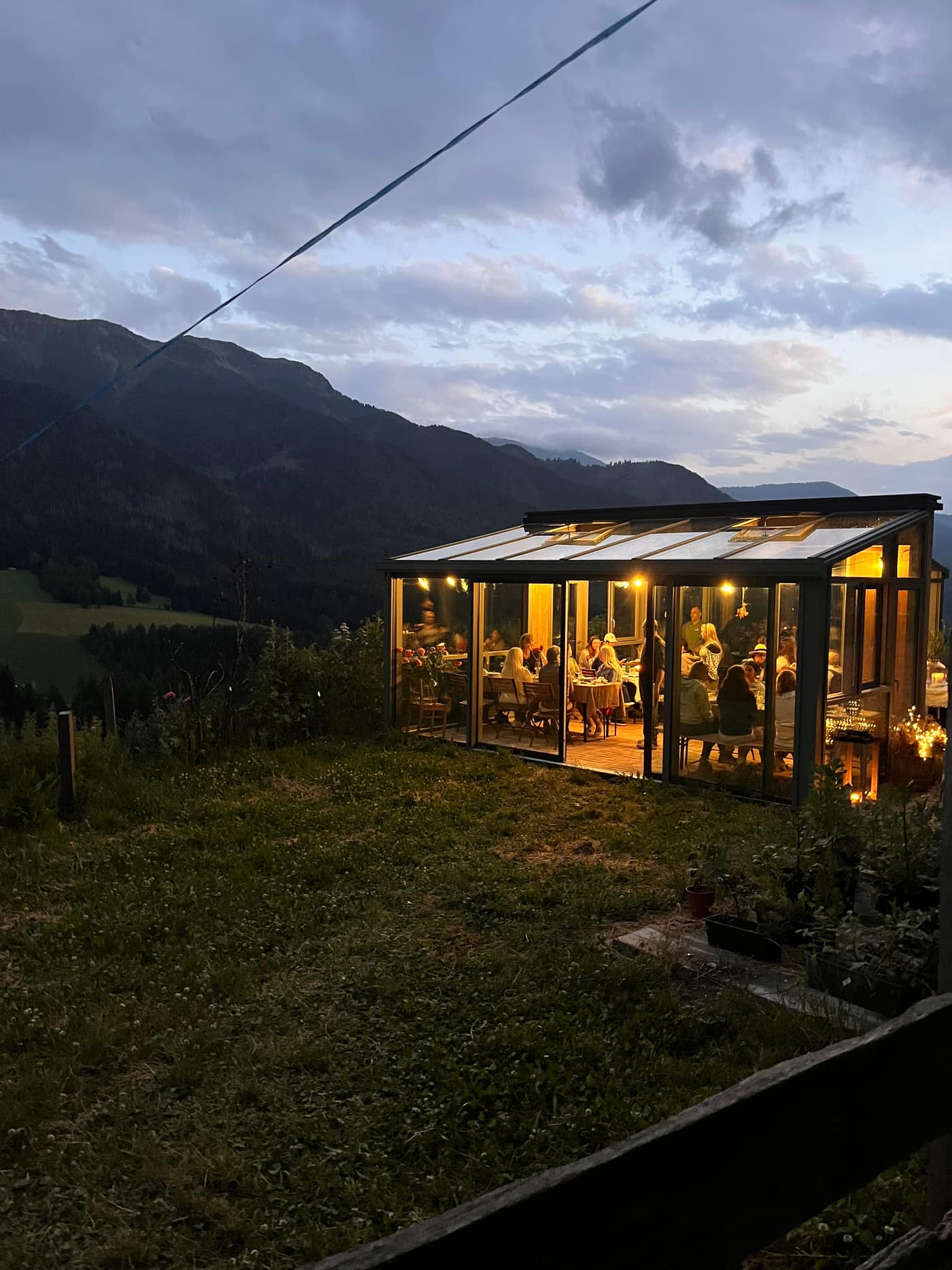 Glashaus bei Dämmerung mit warmem Licht, Berg-Silhouette im Hintergrund